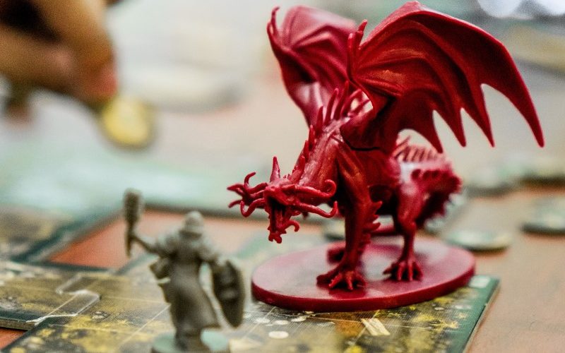 A red plastic dragon mini menaces a gray plastic warrior mini.